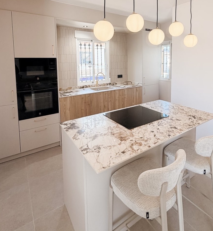 Modern white fitted kitchen with marble-effect island worktop, integrated hob, pendant lights and built-in oven, designed and installed by Kosta Kitchens